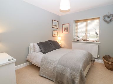 A bedroom with a bed grey pillows and blanket a window with blinds and decorative items 10 Pen Llanw Tides Reach Rhosneigr