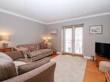 A living room with two sofas a television on a wooden stand and double doors with blinds at 10 Pen Llanw Tides Reach in Rhosneigr