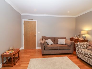 A living room with two sofas a wooden door two wooden tables and a lamp at 10 Pen Llanw Tides Reach in Rhosneigr