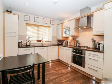 A kitchen with black table and chairs and white cabinets at 10 Pen Llanw Tides Reach in Rhosneigr
