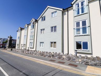 A street view of a residential building with multiple windows and stone wall at 10 Pen Llanw Tides Reach in Rhosneigr