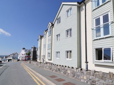 A street with modern houses and a stone clock tower in the distance at 10 Pen Llanw Tides Reach in Rhosneigr