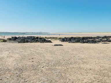 A sandy beach with rocks and people near the shoreline at 10 Pen Llanw Tides Reach in Rhosneigr