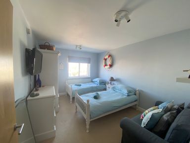 A bedroom with two single beds a sofa and a wall mounted television at 10 Pen Llanw Tides Reach in Rhosneigr
