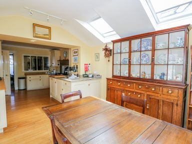 A kitchen and dining area with wooden table and chairs a glass cabinet with dishes and skylights at The White House in Cartmel