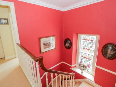 A staircase with white balustrade and wooden handrail beside a window with stained glass and flowers at The White House in Cartmel