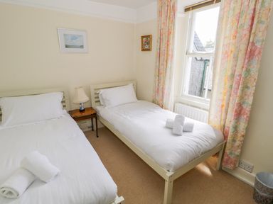 A bedroom with two single beds white bedding towels bedside table lamp and floral curtains at The White House in Cartmel