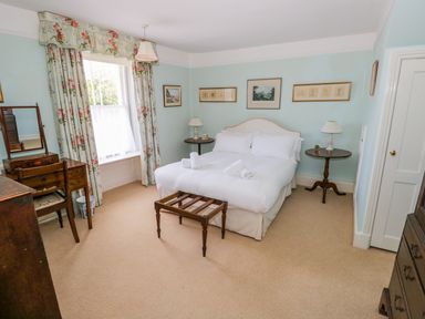 A bedroom with a double bed white bedding side tables lamps a wooden vanity table and floral curtains at The White House in Cartmel
