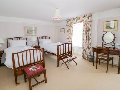 A bedroom with two single beds a wooden dresser with a mirror and floral curtains at The White House in Cartmel