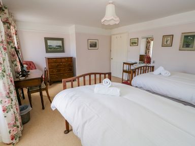 A bedroom with two single beds a wooden dresser a desk and chair framed pictures on the walls and floral curtains at The White House in Cartmel