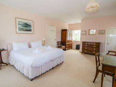 A bedroom with a large bed two chairs a wooden wardrobe and chest of drawers at The White House in Cartmel