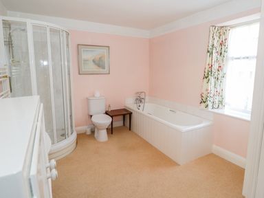 A bathroom with a shower enclosure toilet bathtub and a window with floral curtains at The White House in Cartmel