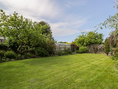 A garden with a green lawn trees shrubs and a wooden shed at The White House in Cartmel