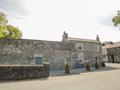 A stone building with green doors and four potted plants on a gravel area by a road at The White House in Cartmel