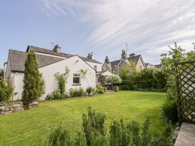 A garden with grass and plants behind a white house with other houses in the background at The White House in Cartmel