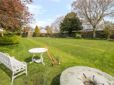 A garden with a white metal bench and table croquet equipment and trees at The White House in Cartmel