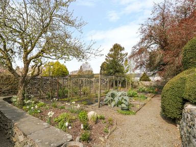 A garden with flower beds trees and a fenced vegetable patch at The White House in Cartmel