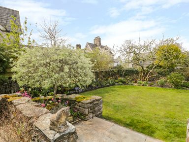A garden with a grass lawn and stone wall with a small tree and flowers at The White House in Cartmel