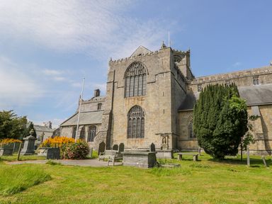 An exterior view of a stone church with tall arched windows surrounded by grass benches and gravestones