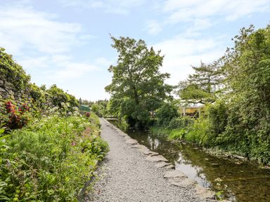 A gravel path alongside a shallow river with bushes and trees on both sides at The White House in Cartmel