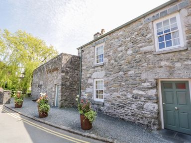 A stone building with potted plants outside along a gravel area at The White House in Cartmel