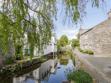 A narrow stone bridge over a calm water canal with stone and white buildings alongside and green leafy trees at The White House in Cartmel