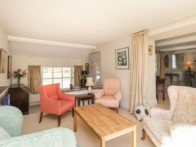 A sitting room with armchairs and a wooden table near a window with curtains at The White House in Cartmel