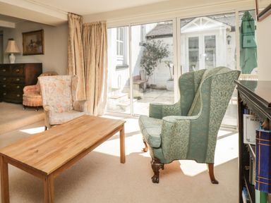 A living room with a wooden coffee table two armchairs sliding glass doors and a chest of drawers at The White House in Cartmel