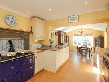 A kitchen with cream cabinets a blue stove and wooden dining table with chairs at The White House in Cartmel