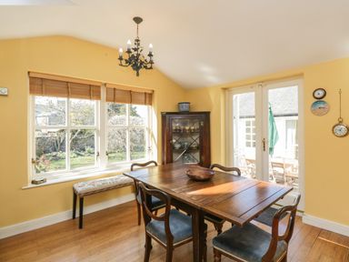 A dining room with a wooden table and chairs near windows and glass doors at The White House in Cartmel