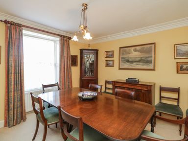 A dining room with wooden table and chairs a corner cabinet paintings and curtains at The White House in Cartmel