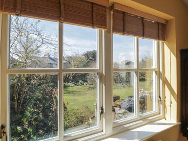 A window with wooden blinds overlooking a garden with grass and trees at The White House in Cartmel