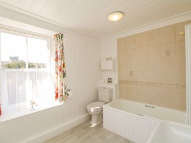 A bathroom with a bathtub toilet floral curtains and a window at The White House in Cartmel