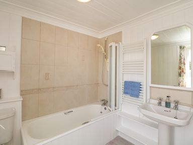 A bathroom with a bathtub shower combination a white sink with a mirror above and a towel rack with a blue towel at The White House in Cartmel