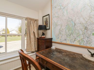 A study room with a wooden desk chair a chest of drawers with a lamp and large framed map on the wall at The White House in Cartmel