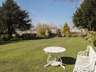 A garden with a white metal table and bench on the grass and trees in the background at The White House in Cartmel