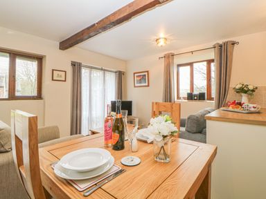 A dining table set with plates glasses and bottles next to a living area with sofas and windows at Hilly Field Barn in Yelverton