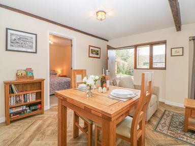 A dining area with a wooden table set for two near an open door and a sofa at Hilly Field Barn in Yelverton