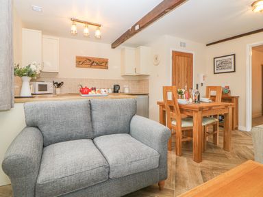 A kitchen and dining area with a grey sofa wooden dining table and chairs at Hilly Field Barn in Yelverton