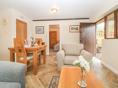 A living area with a wooden dining table and chairs a beige armchair and a coffee table with flowers visible at Hilly Field Barn in Yelverton