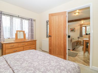 A bedroom with a wooden dresser mirror floral curtains and a bed opening into a living area at Hilly Field Barn in Yelverton