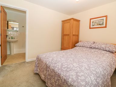A bedroom with a bed covered in a floral bedspread a wooden wardrobe and an open door leading to a bathroom at Hilly Field Barn in Yelverton