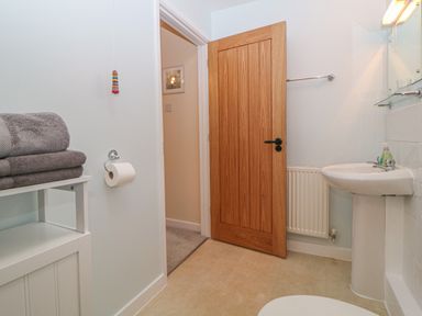A bathroom with a wooden door a pedestal sink towels on a shelf and a toilet paper holder at Hilly Field Barn in Yelverton