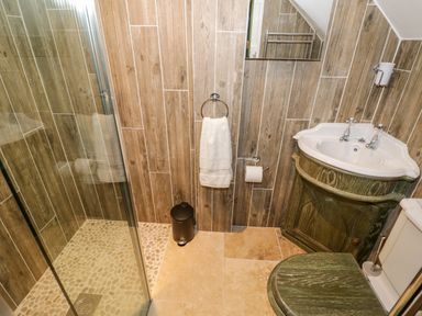 A bathroom with a glass shower enclosure towel rack sink with wooden cabinet and toilet at The Old Paper Shop in Tewkesbury