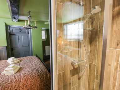 A bedroom with a bed and folded towels beside a shower with wooden tile walls at The Old Paper Shop in Tewkesbury