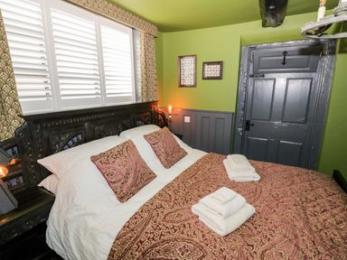 A bedroom with a bed with patterned pillows and bedspread green walls and a grey door at The Old Paper Shop in Tewkesbury