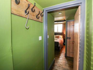 A hallway with green walls and wooden coat hooks leading to a bedroom with a wooden floor and a bed at The Old Paper Shop in Tewkesbury