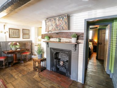 A room with a fireplace a wooden table with chairs and plants visible bedroom through doorway at The Old Paper Shop in Tewkesbury
