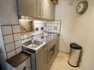 A small kitchen with a stainless steel sink stove and oven a silver trash can and a wall clock at The Old Paper Shop in Tewkesbury