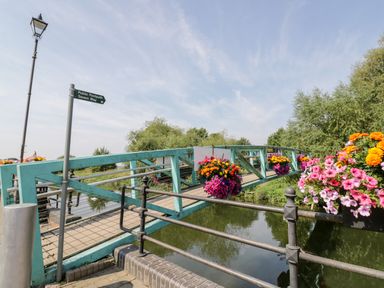 A turquoise pedestrian bridge with flower baskets over a river and a signpost for public footpath Severn Way at The Old Paper Shop in Tewkesbury